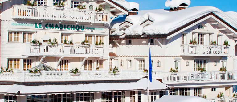 Hotel branco alpino com varandas decoradas e neve ao redor.