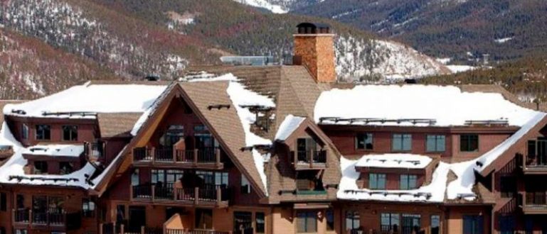 Fachada do Crystal Peak Lodge com edifício rústico e montanhas nevadas ao fundo.