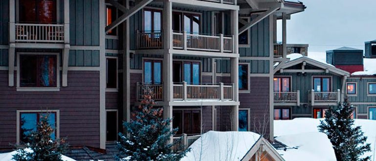 Fachada iluminada do resort Four Seasons em Jackson Hole com neve ao redor.