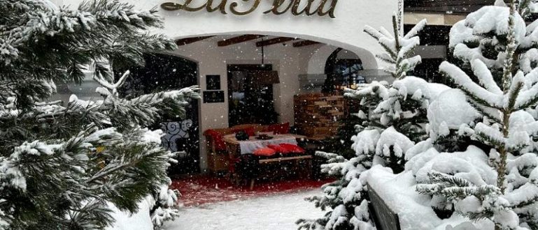 Entrada do Hotel La Perla cercada por árvores cobertas de neve.