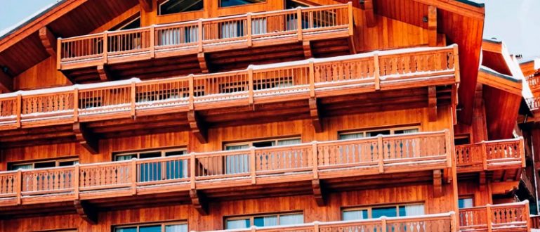 Fachada do Le Coucou com varandas de madeira e neve no telhado.