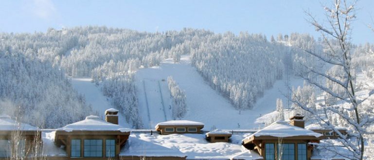 Hotel em frente a uma montanha de esqui, cercado por neve e árvores.