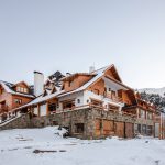 Hotel de montanha em estilo chalé com fachadas de madeira e pedra, coberto de neve.