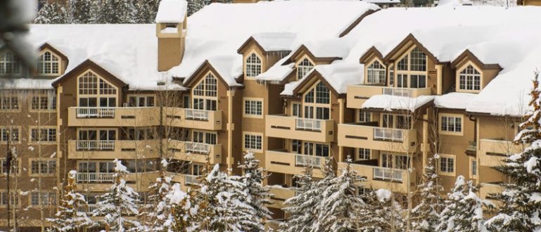 Resort de montanha com telhados cobertos de neve, cercado por árvores nevadas.