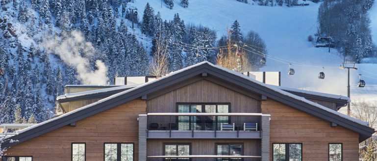 O W Aspen Hotel com fachada moderna e um cenário de montanha nevada ao fundo.