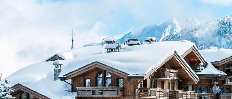 Hotel de madeira com varandas, teleférico passando ao lado, cercado de neve.